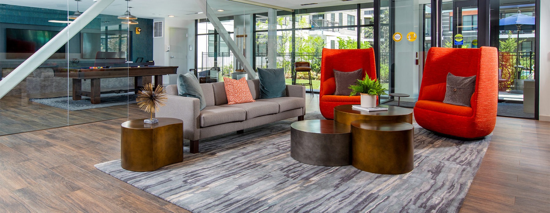 Resident lounge with red chairs, couches, and end tables. Floor-to-ceiling windows look out to courtyard