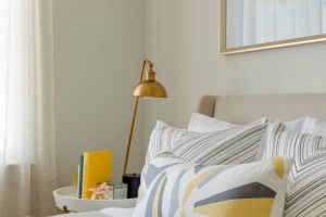 Close up on queen-sized bed with designer pillow, wall art and gold lamp