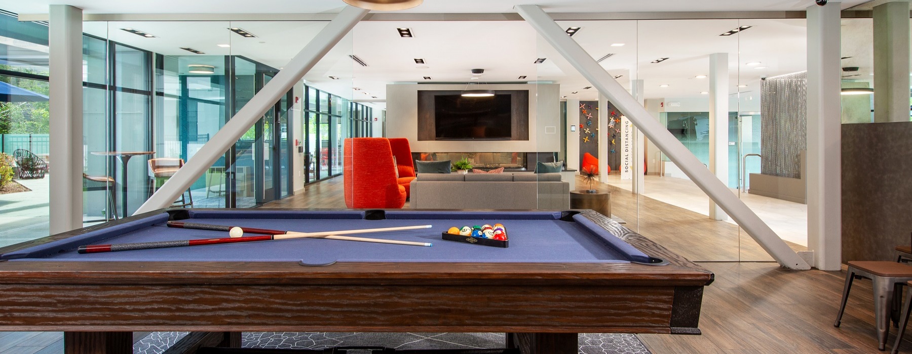 game room with pool table, lighting, flat screen TV and seating. View to outdoor seating area. 